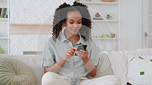 Smiling African American teen girl holding smart phone in living room.