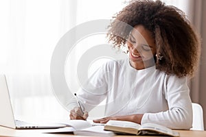 Smiling African American teen girl preparing school homework, using laptop