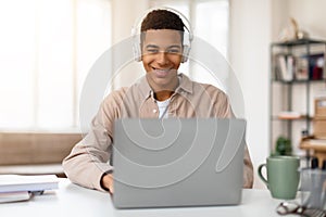 Smiling african american teen guy with headphones using laptop
