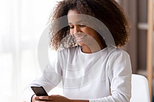 Smiling African American teenage girl using phone, looking at screen