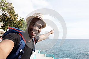 Smiling african american travel man taking selfie by the sea and pointing finger