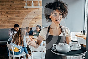 Smiling african american waitress holding tray with tea and customers sitting behind her photo