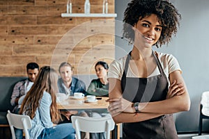 Smiling african american waitress standing with customers sitting behind photo