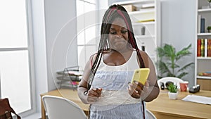 Smiling african american woman boss gives a thumb-up gesture while working on her phone in the office, embodying elegance and