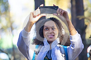 Smiling African American woman in the forest taking a selfie on a smartphone.