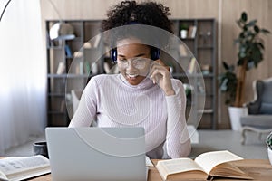 Smiling African American woman in headphones using laptop, watching webinar