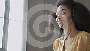 Smiling African American woman with headset using laptop, talking, working customer support service operator at hom