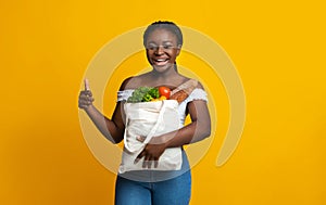 Smiling african american woman holding bag with groceries and showing thumb up