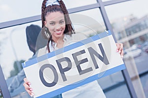 Smiling african american woman holding an Open sign in front of modern