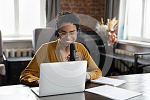 Smiling African American woman recording audio in professional stand microphone.