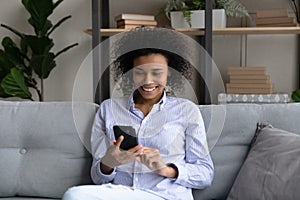 Smiling African American woman relaxing on couch with smartphone