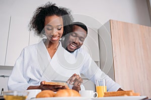 Smiling african american woman spreading butter on toast with boyfriend