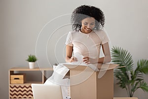 Smiling African American woman unpacking parcel, removing bubble wrap