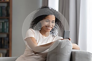 Smiling African American woman using cellphone, relaxing on couch