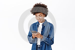Smiling african american woman using mobile phone, holding telephone and looking happy, standing over white background