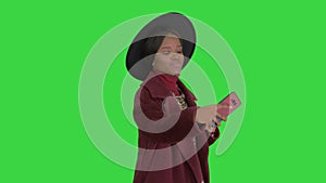 Smiling african american woman wearing fashion coat and a black hat taking selfie while walking on a Green Screen