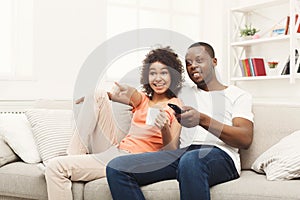 Smiling african-american young couple watching TV at home