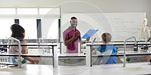 Smiling african american young male teacher gesturing while reading file to multiracial students