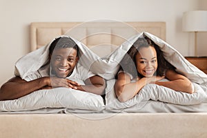Smiling African American Young Spouses Lying Under Blanket In Bed