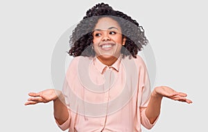 Smiling African American young woman shrug shoulders, looks uncertain, confused with open hand palms, has doubts. Dark-skinned