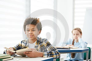 Smiling African Boy Holding Book in School Classroom