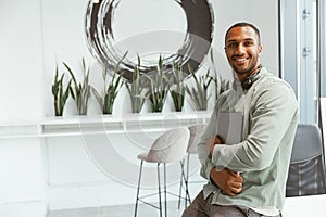 Smiling african businessman holding laptop while sitting in cozy office