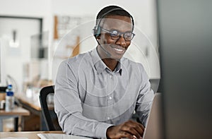 Smiling African businessman talking on a headset and using a laptop