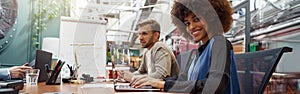 Smiling african businesswoman sitting on his workplace in modern office on colleague background