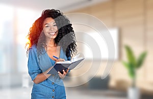 Smiling african businesswoman taking notes, blurred office room