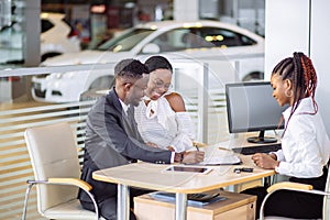 African couple getting car key from dealer in showroom and signing contract