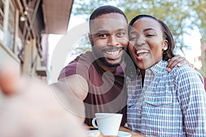 Smiling African couple taking selfies together at a sidewalk cafe