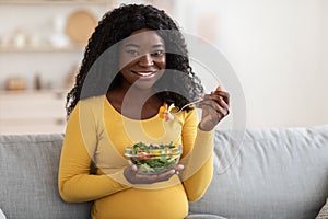 Smiling african expecting woman eating vegetable salad