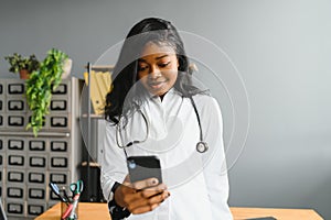 Smiling african female doctor physician holding cell phone talking on mobile at work. Healthcare professional answering