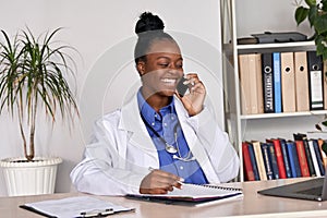 Smiling african female doctor physician holding phone talking on mobile at work.