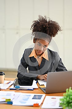 Smiling African female manager using laptop and working with financial docent in her personal office