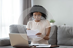 Smiling african girl student reading paper letter sit on sofa