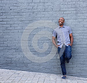 Smiling african guy leaning against gray wall