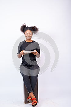 Smiling african lady using a tablet computer, sitting against a white backdrop