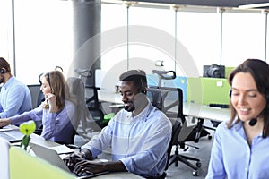 Smiling african male call-center operator with headphones sitting at modern office with collegues on the backgroung