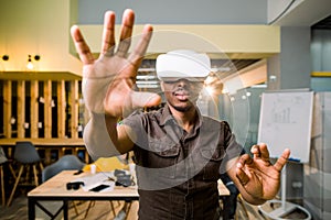 Smiling african man enjoying virtual reality glasses while standing in modern office. Happy young guy with vr headset or