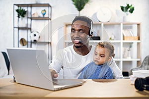 African man with son on knees working on laptop at home