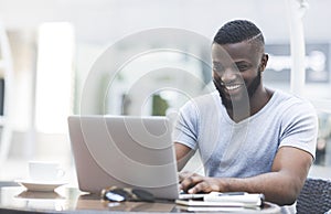 Smiling african man textmessaging on laptop in cafe