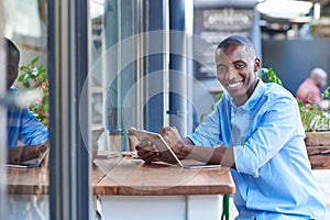 Smiling African man working online at a sidewalk cafe counter