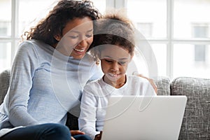 Smiling african mother and kid daughter have fun with laptop