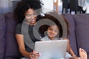 Smiling african mother and kid daughter having fun with computer