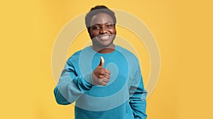 Smiling African showing cool thumb up gesture like good job positive choice posing isolated orange