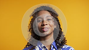 Smiling african woman with finger on lips - shhh, secret, silence, yellow studio