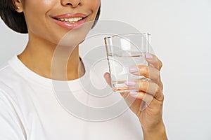 Smiling african woman hold glass of still water. Water balance and caring for skin and body concept