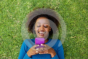 Smiling african woman lying on grass looking at cell phone