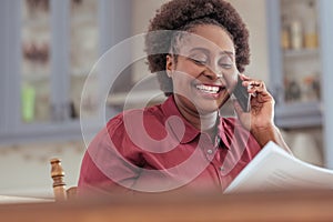 Smiling African woman reading paperwork and talking on her cellphone